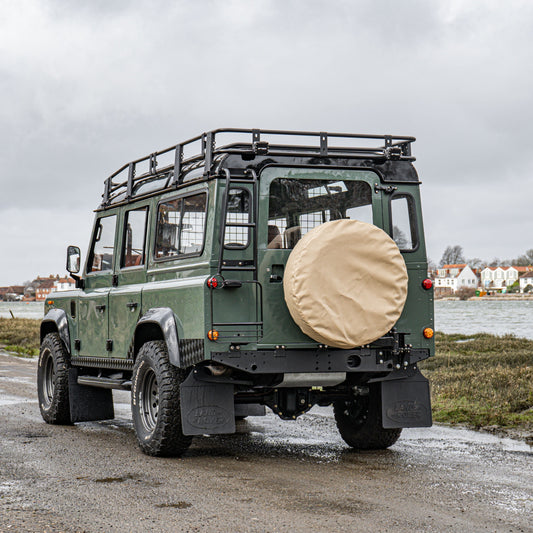green land rover 110 with canvas wheel cover at coast