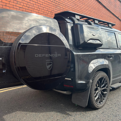 Land rover Defender With New Aquarius Manufacturing C mould Spare Wheel Cover, door open, red brck wall behind, sunny day