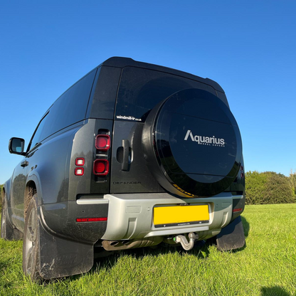 Land rover Defender With New Aquarius Manufacturing C mould Spare Wheel Cover, parked in green grass field, sunny day, clear blue sky